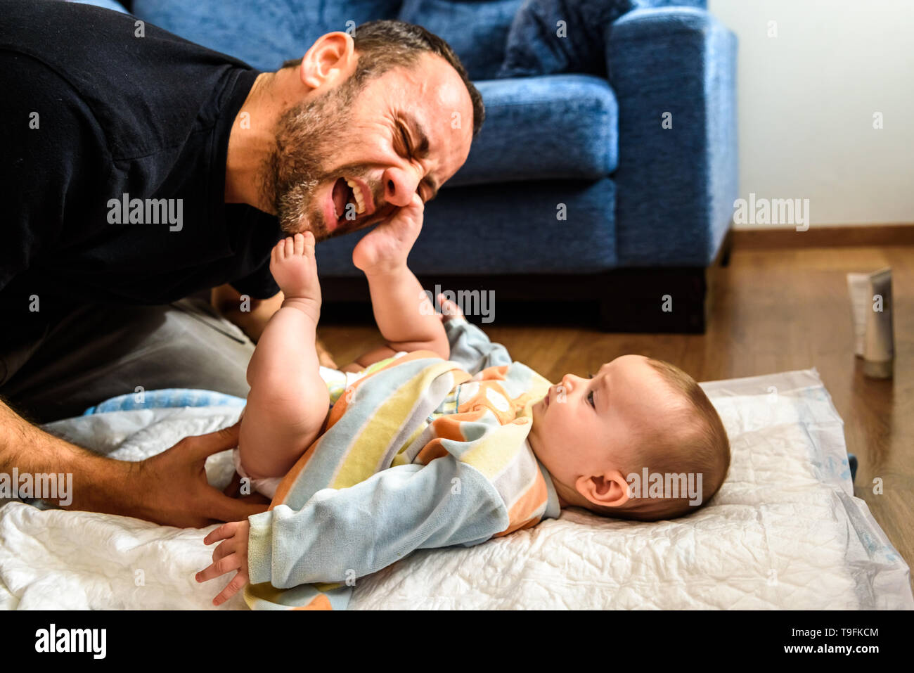 Dad struggling with his baby daughter to change dirty diapers putting faces of effort, concept