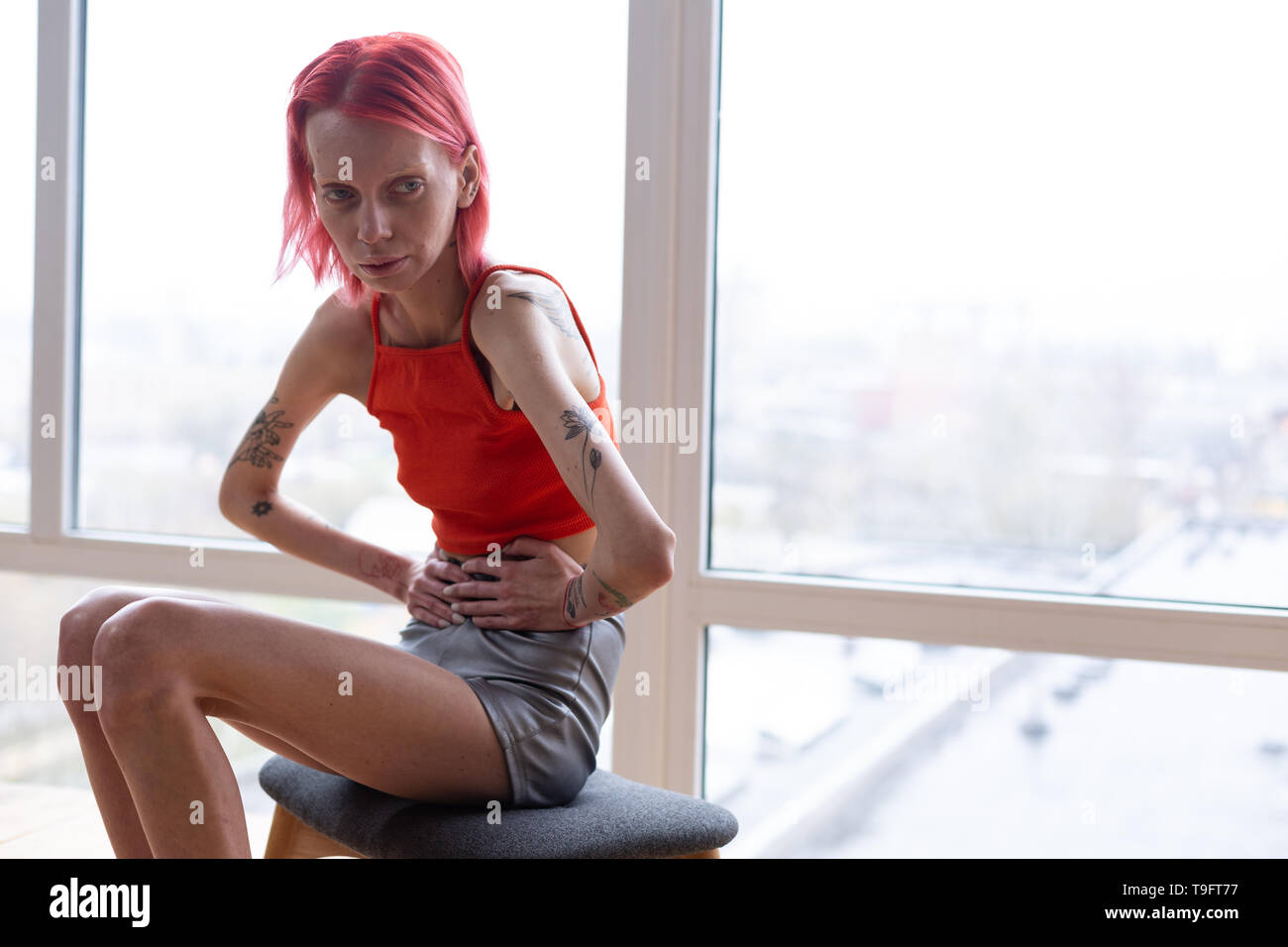 Woman with anorexia sitting near the window feeling awful Stock Photo