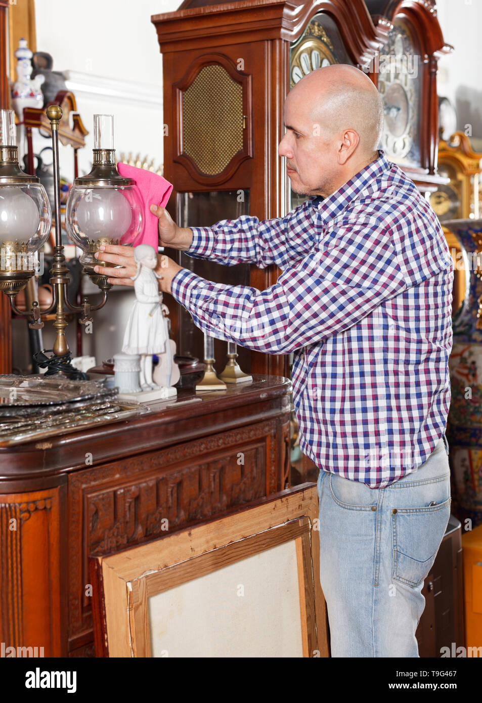 Mature male working in antique store carefully wiping dust on antique lamp Stock Photo