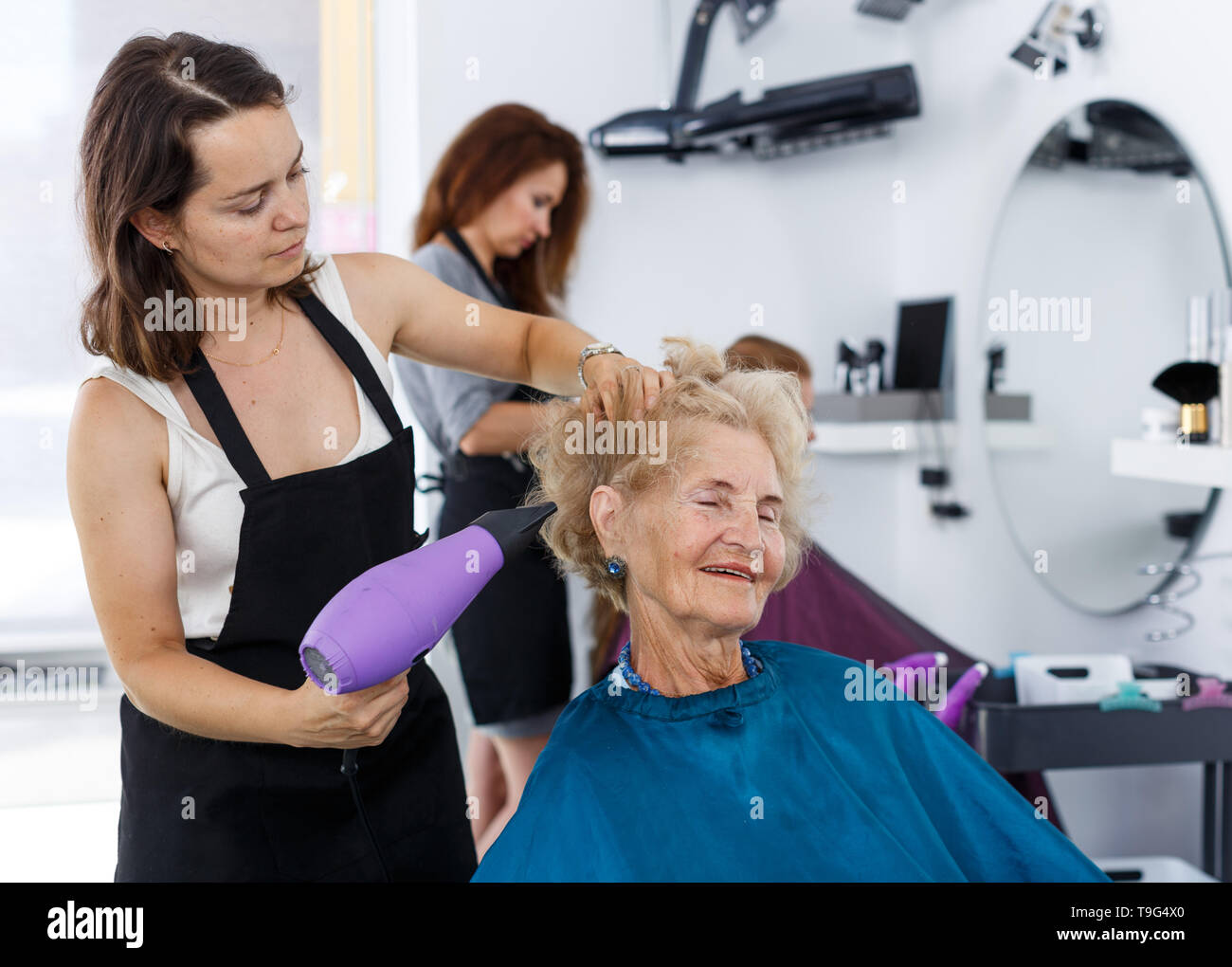 Professional Female Stylist Making Hairdo For Senior Woman In