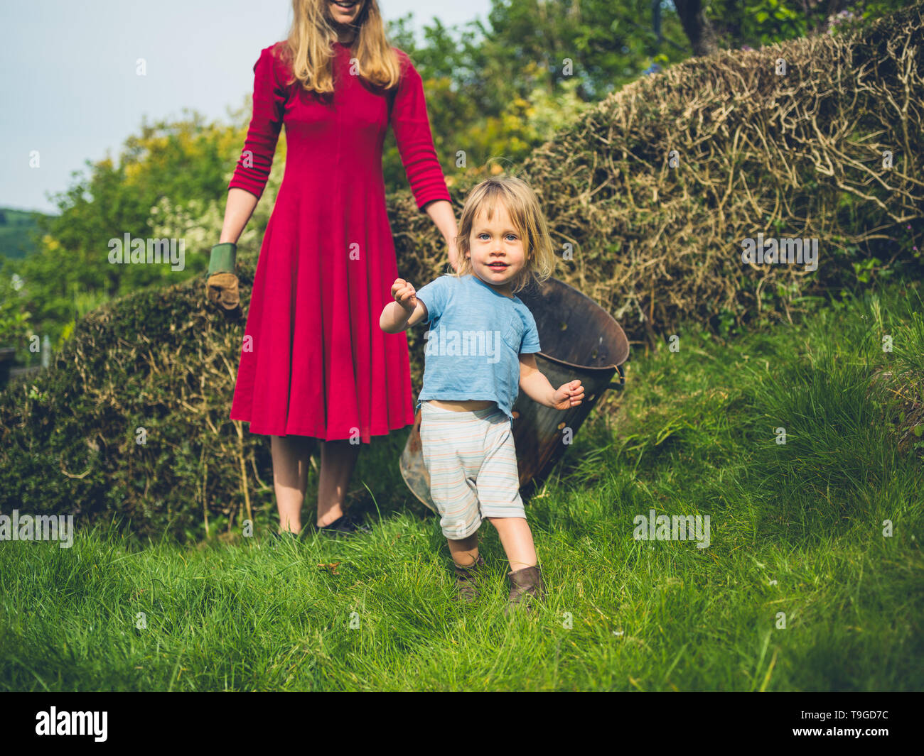 A little toddler is dancing and posing in the garden with his mother in the background Stock Photo