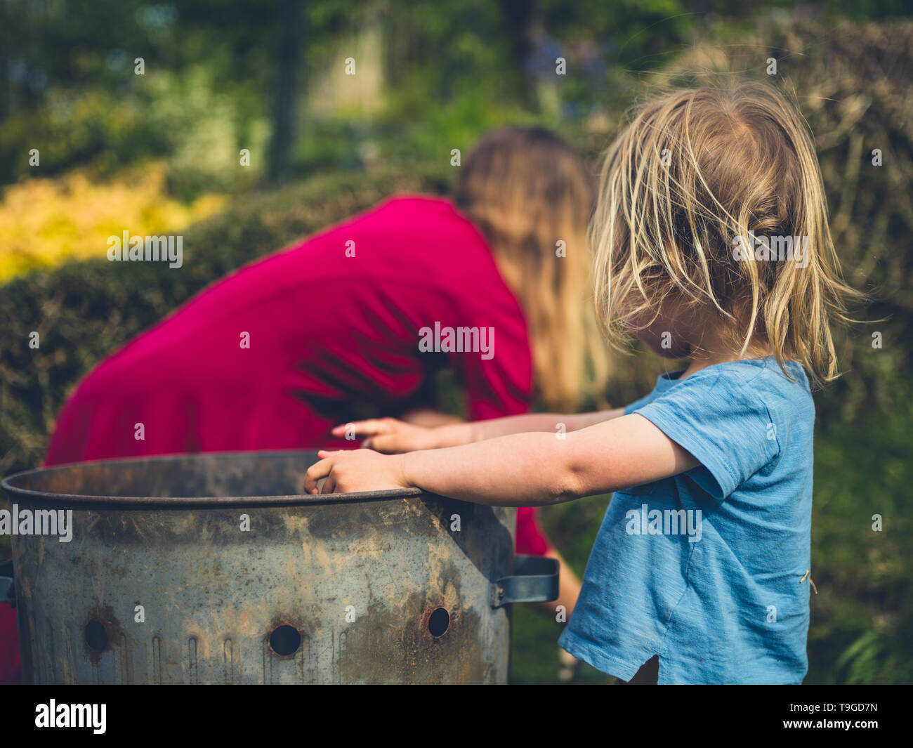 A little toddler is helping his mother put weeds in an incinerator ...