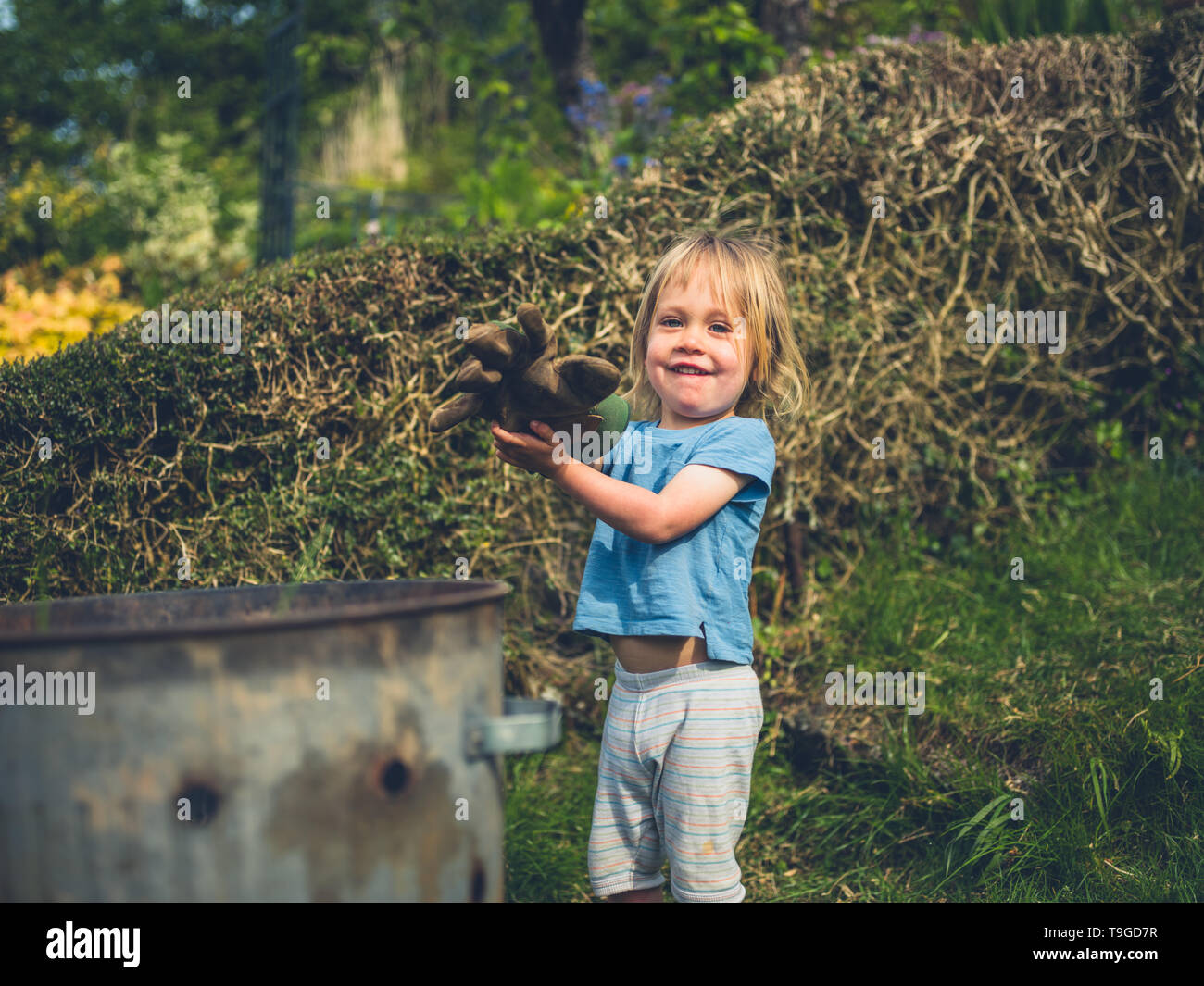 A little toddler is gardening and putting weeds in an incinerator Stock Photo