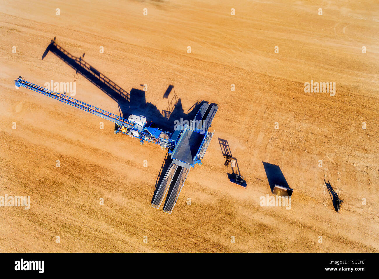 Grain bulk storage elevator site with mechanical loader processing tonnes of wheat and other grains in aerial overhead top down view. Stock Photo