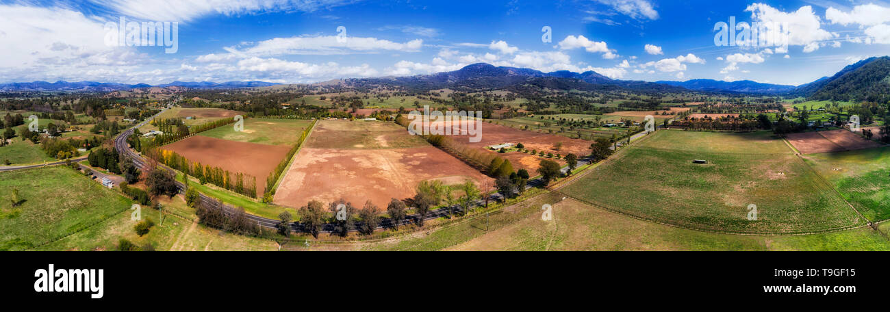 New England highway through green valley of upper Hunter Valley and horse farms between distant hill ranges - wide aerial panorama. Stock Photo
