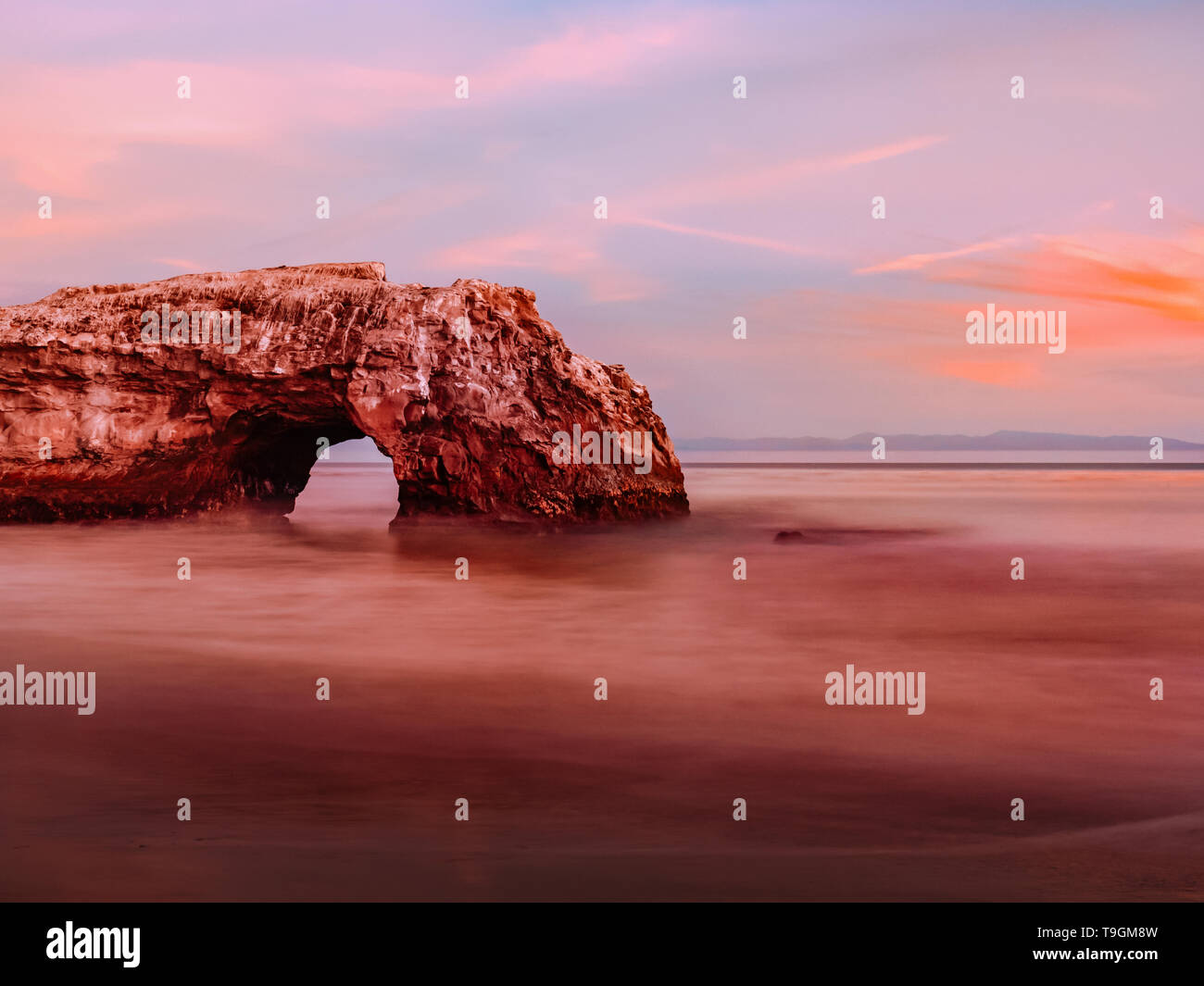 Natural rock arch on the Pacific Ocean beach in long exposure Stock Photo