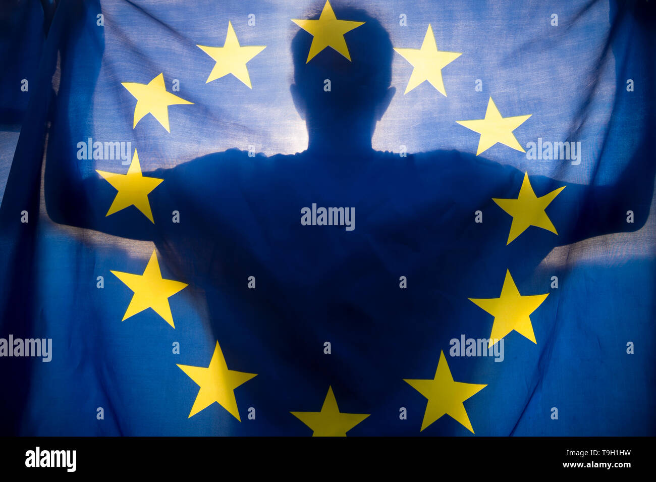 Shadow silhouette of a man holding an EU European Union flag backlit by the rising sun Stock Photo