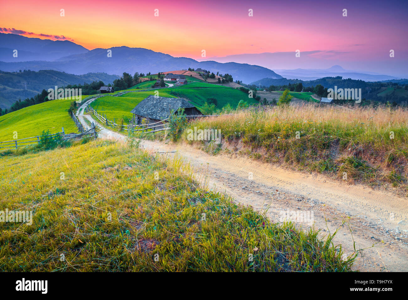 Amazing travel location, summer countryside landscape, green fields and wooden houses with gardens at sunset, Bran, Transylvania, Romania, Europe Stock Photo