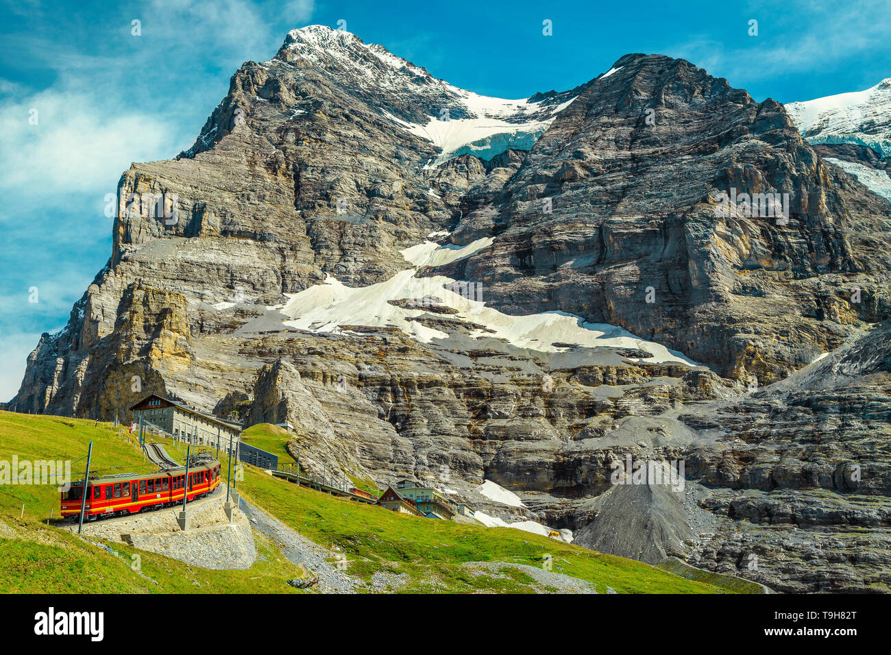 Stunning summer travel experience, popular electric red tourist train Jungfraujoch and snowy mountains in background, near Kleine Scheidegg station, B Stock Photo