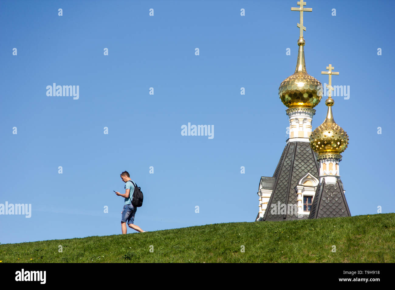 Young man wearing back pack walking in front of Assumtion cathedral and looking at smartphone. Stock Photo