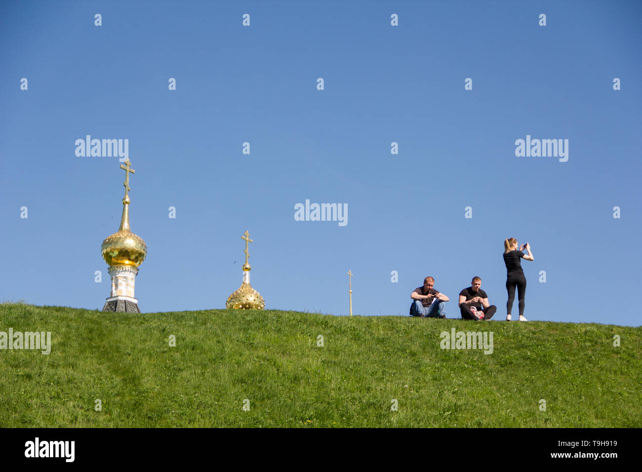 Two young men and young woman relaxing on the ground in front of Assumption cathedral. Stock Photo