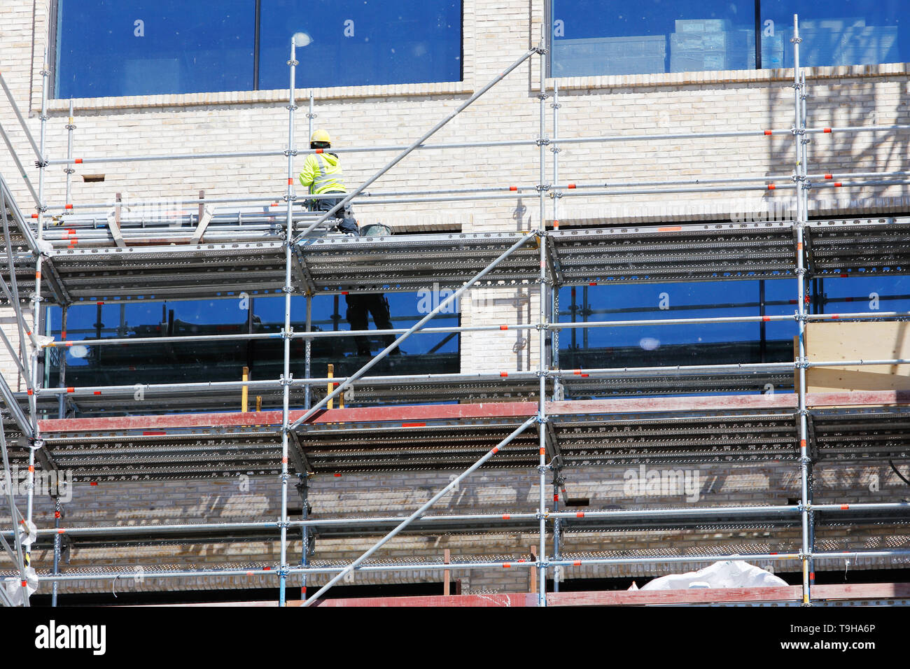 A new building under construction with a worker standing on the scaffolding. Stock Photo