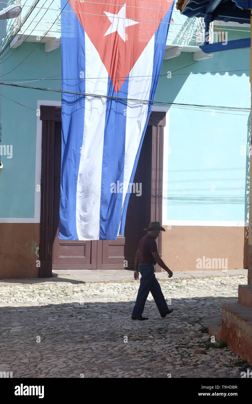 A man in a cowboy hat walks past a Cuban flag in Trinidad, Cuba Stock Photo