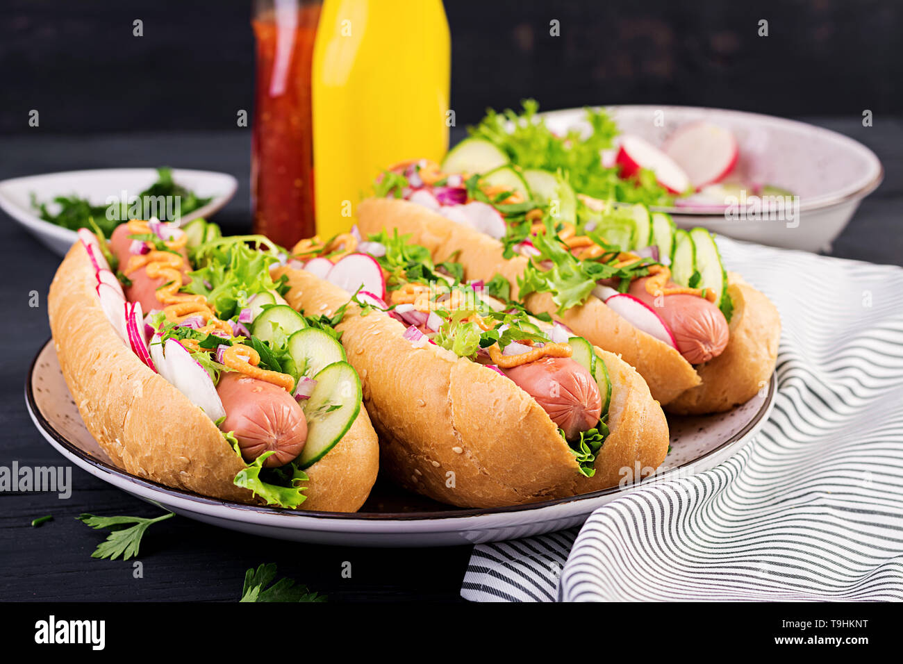 Hot dog with sausage, cucumber, radish and lettuce on dark wooden