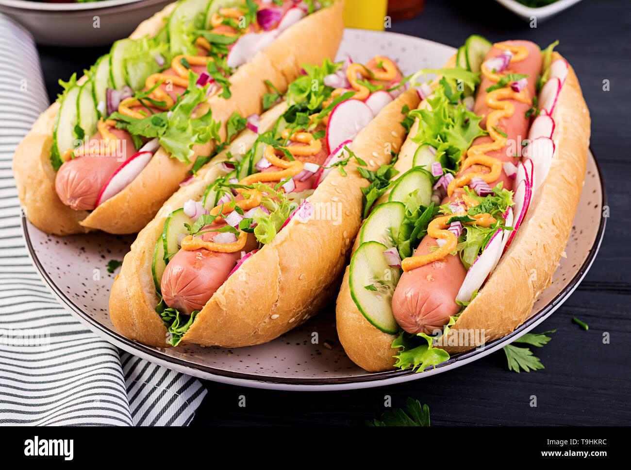 Hot dog with sausage, cucumber, radish and lettuce on dark wooden