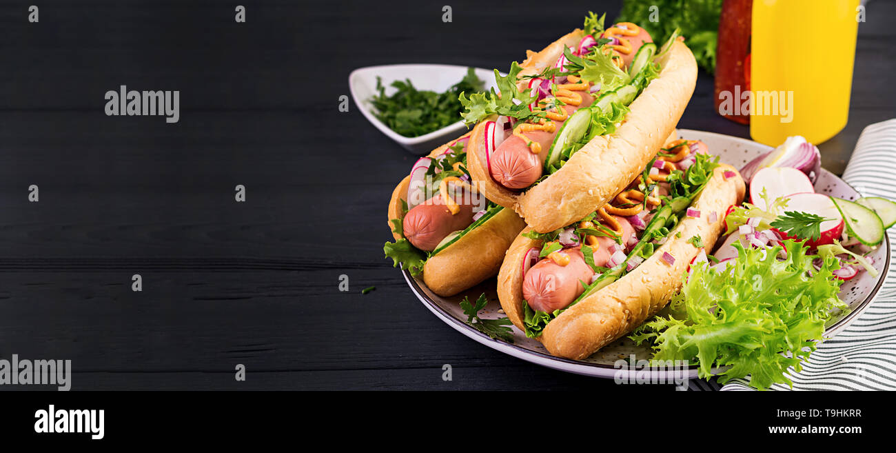 Hot dog with sausage, cucumber, radish and lettuce on dark wooden