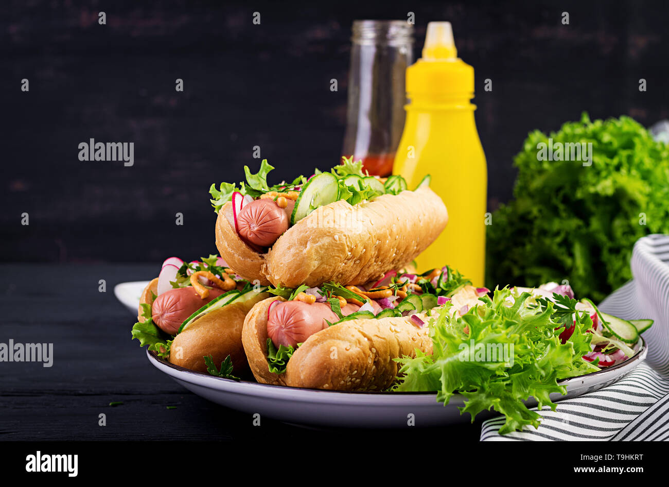 Hot dog with sausage, cucumber, radish and lettuce on dark wooden