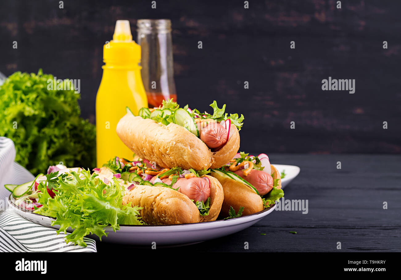 Hot dog with sausage, cucumber, radish and lettuce on dark wooden
