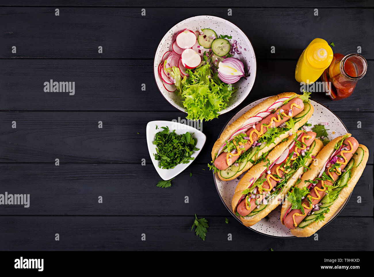 Hot dog with sausage, cucumber, radish and lettuce on dark wooden
