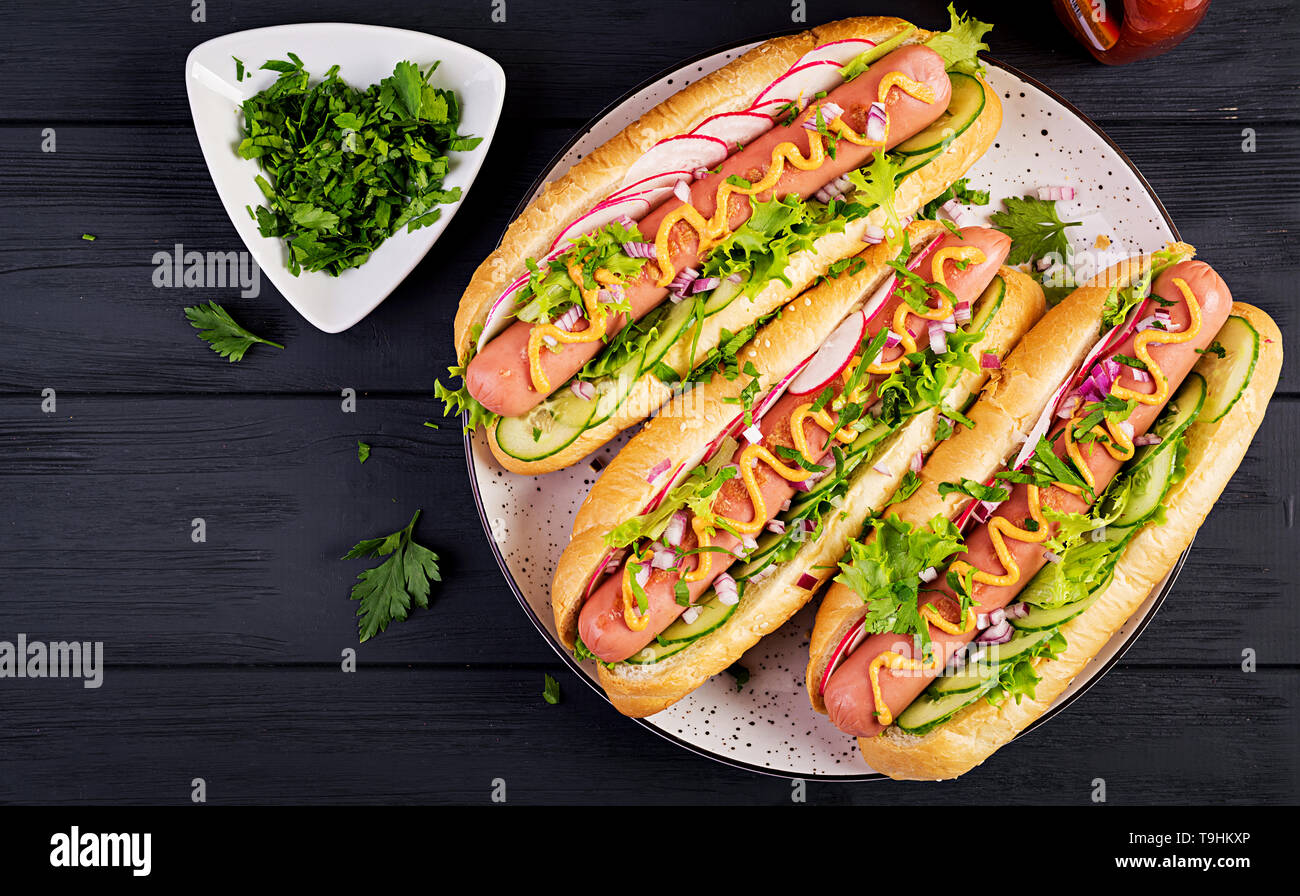 Hot dog with sausage, cucumber, radish and lettuce on dark wooden