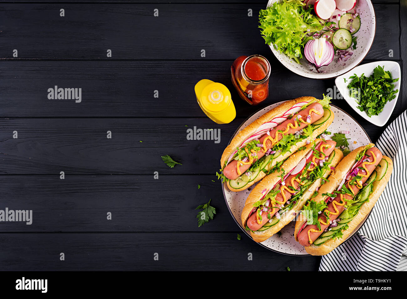 Hot dog with sausage, cucumber, radish and lettuce on dark wooden