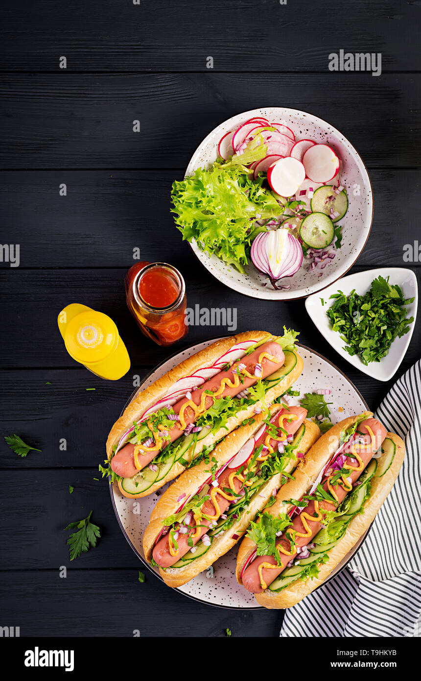 Hot dog with sausage, cucumber, radish and lettuce on dark wooden