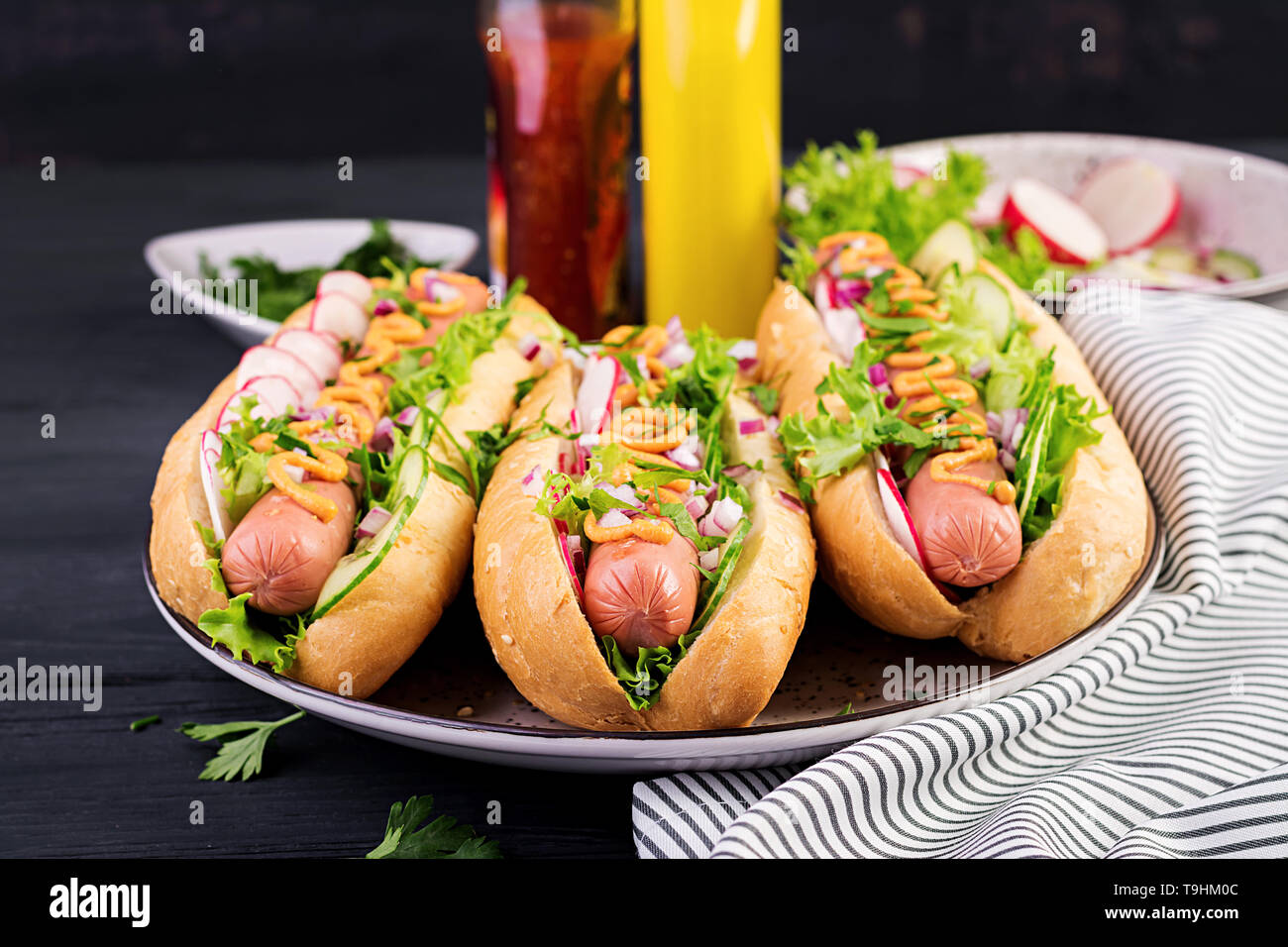 Hot dog with sausage, cucumber, radish and lettuce on dark wooden