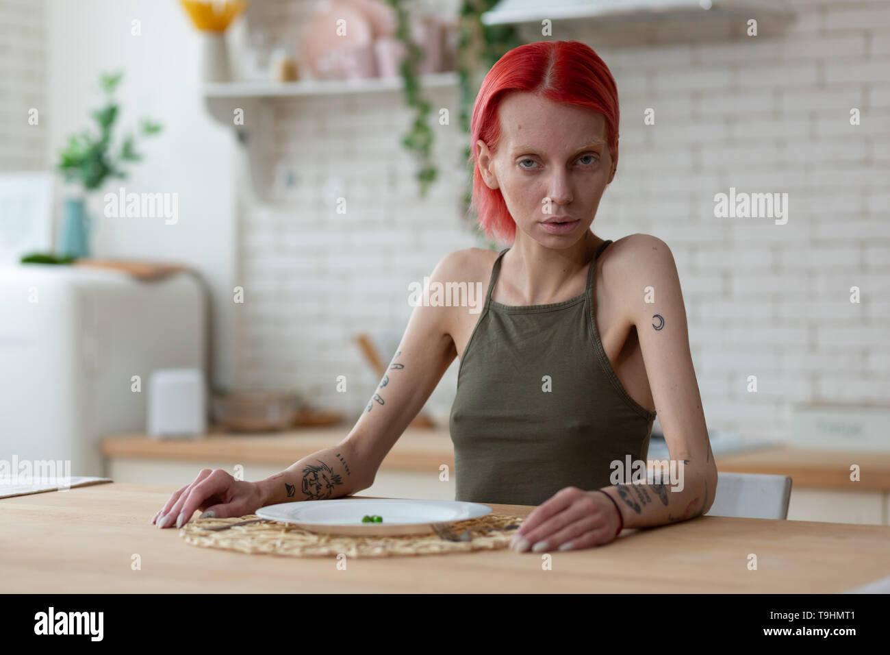 Red-haired anorexic woman sitting in the kitchen alone Stock Photo