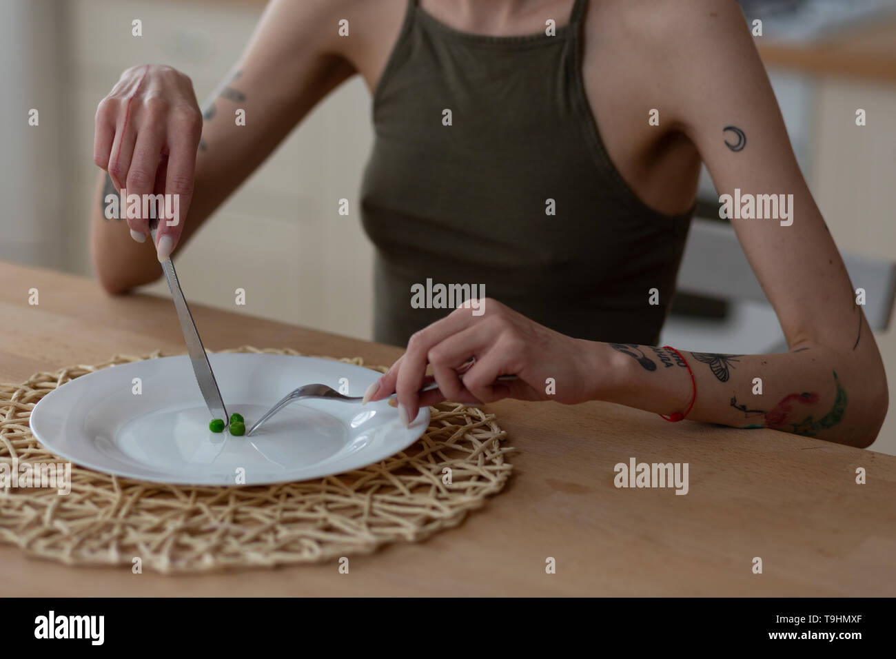 Woman holding knife and fork while eating only three green peas Stock
