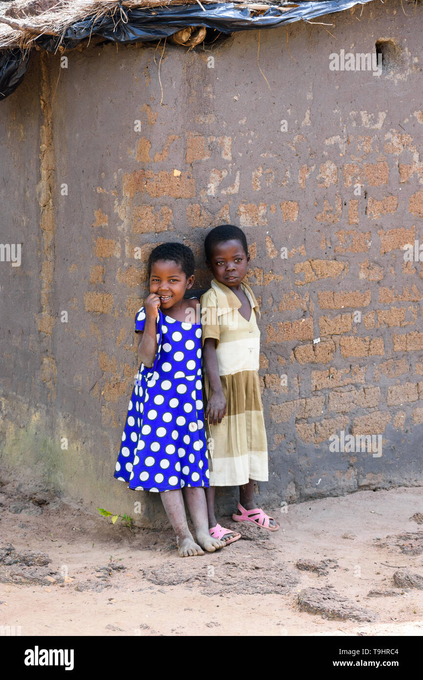 two young Malawian girls stand in the shade of a wall of their mud hut in a village in central Malawi Stock Photo