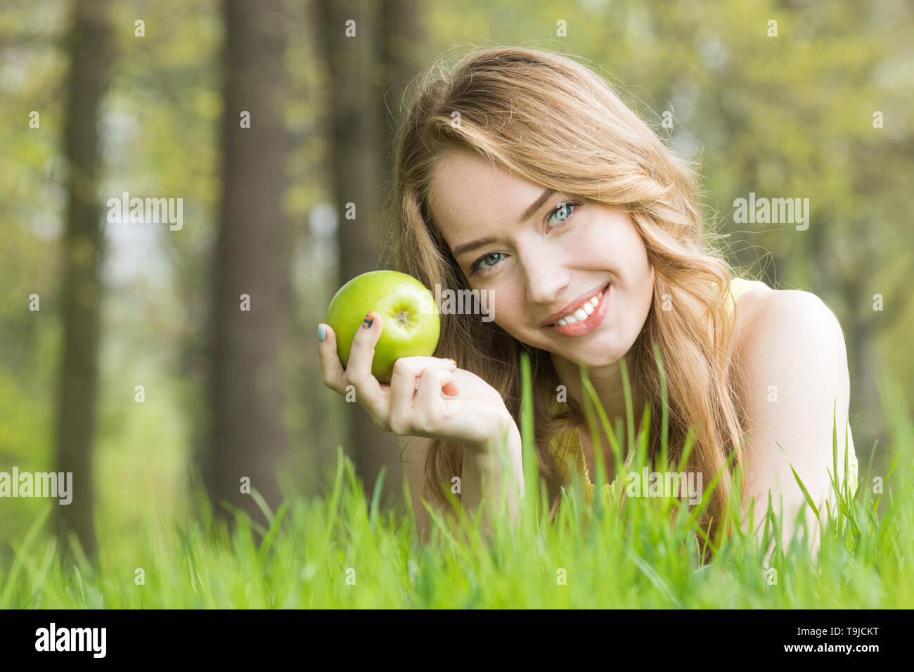 Blonde pretty girl laying on the grass in spring park and smiling ...