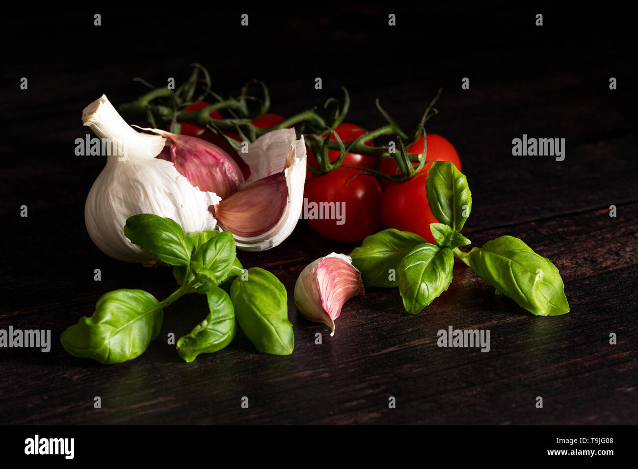 Garlic bulb and cloves with basil and tomatoes on dark board Stock Photo
