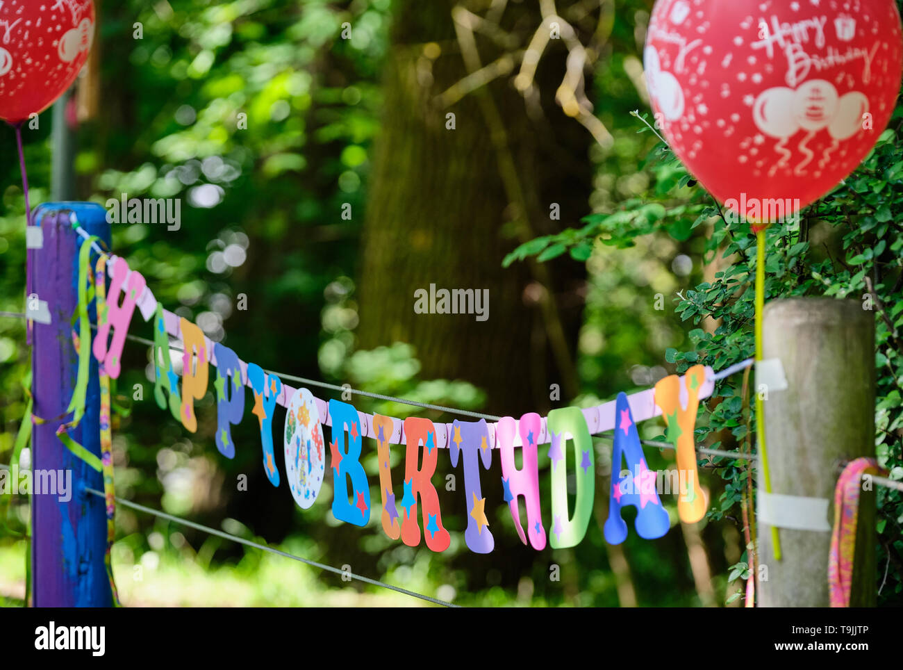 Colorful Happy Birthday paper garland with two red balloons fixed on wooden poles of a fence in