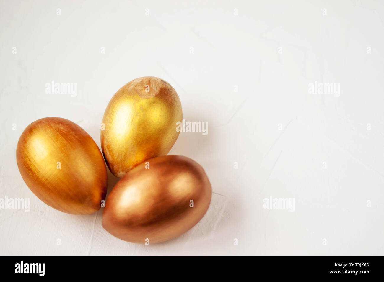 Three gold and bronze Easter eggs on a white background Selective soft focus. Copy space. Stock Photo