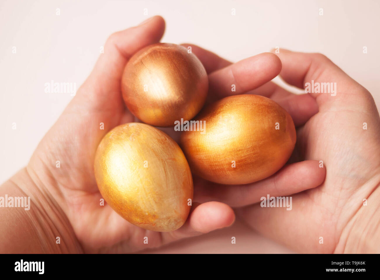 Three bright gold and bronze eggs in hands on a white background, Selective soft focus. Copy space. Stock Photo