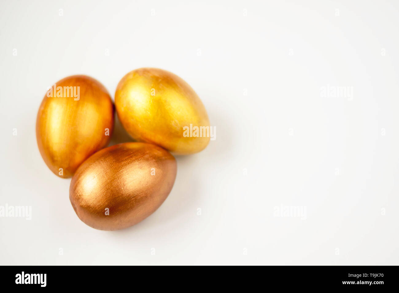 Three gold and bronze Easter eggs on a white background. Selective soft focus. Copy space. Stock Photo