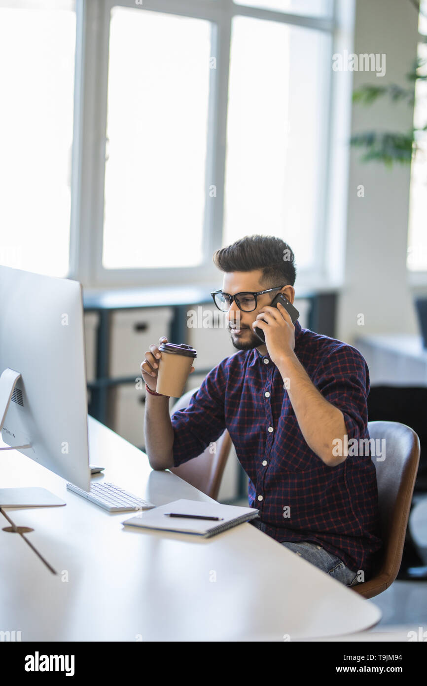 Indian man is working on his computer in the office and talking by ...