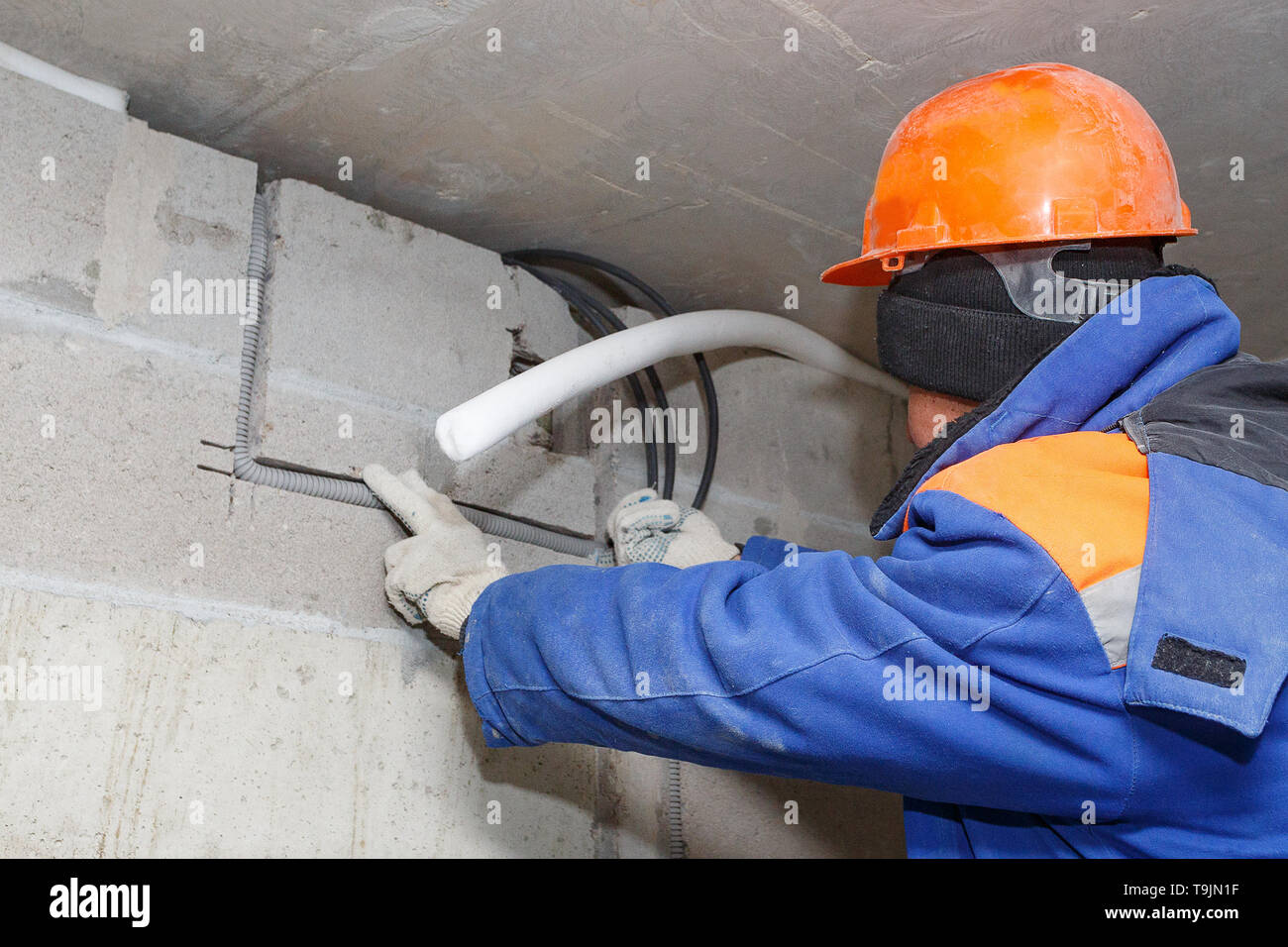 The worker in the helmet is laying electrical wiring during the roughing phase. Stock Photo