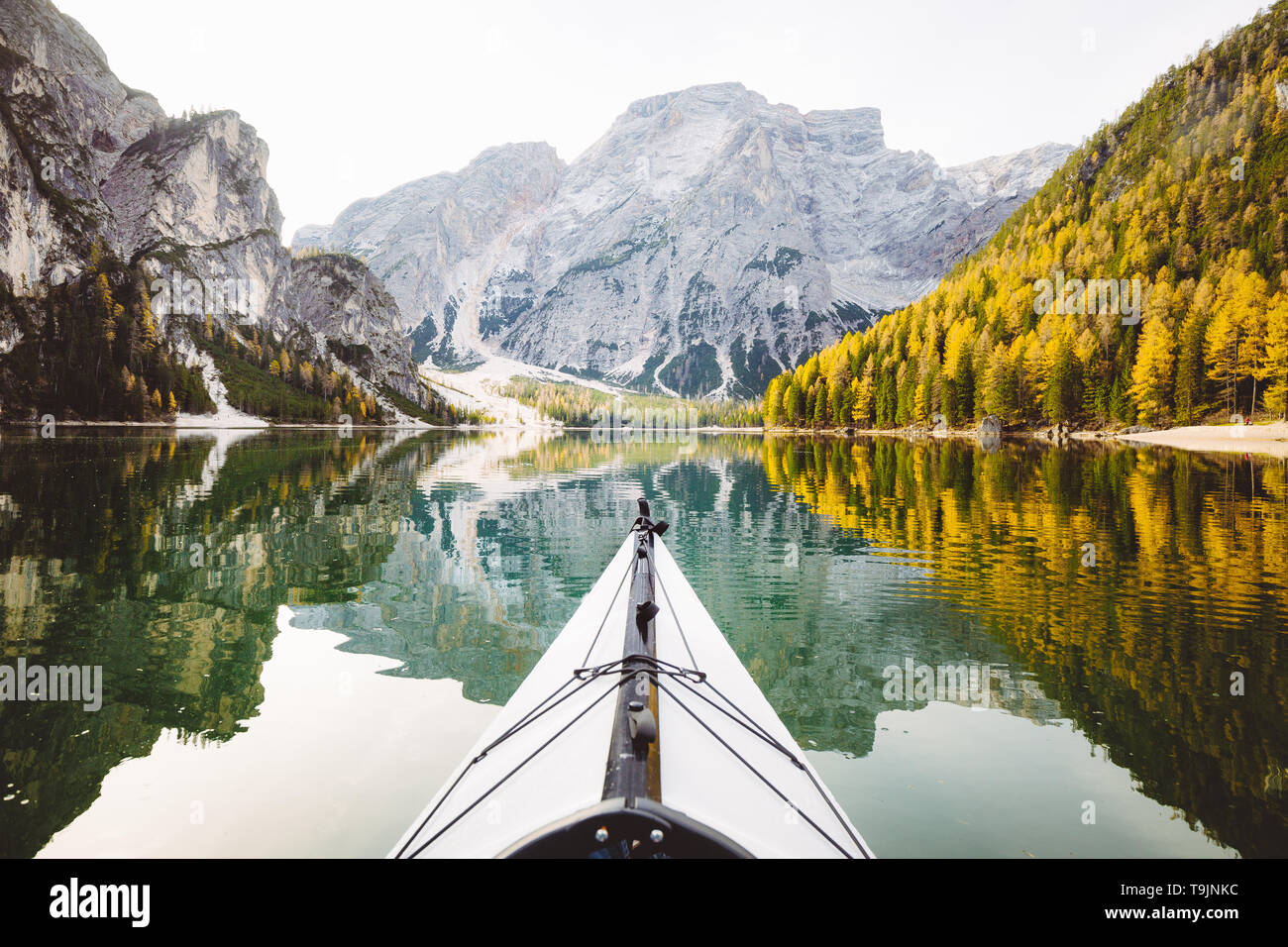 Beautiful view of kayak on a calm lake with amazing reflections of mountain peaks and trees with yellow autumn foliage in fall, Lago di Braies, Italy Stock Photo