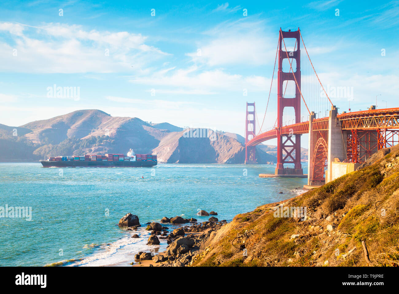 Classic view of famous Golden Gate Bridge with cargo ship on a sunny day with blue sky and clouds in summer, San Francisco, California, USA Stock Photo