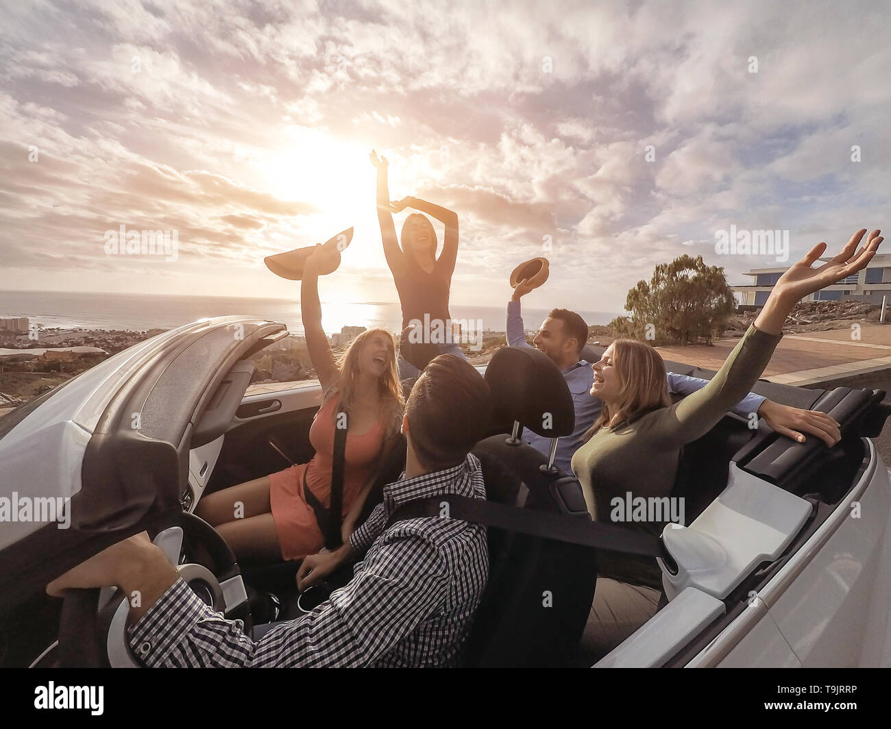 Happy friends with their hands up having fun in cabriolet car on vacation - Young people laughing and enjoying together during travel road trip Stock Photo
