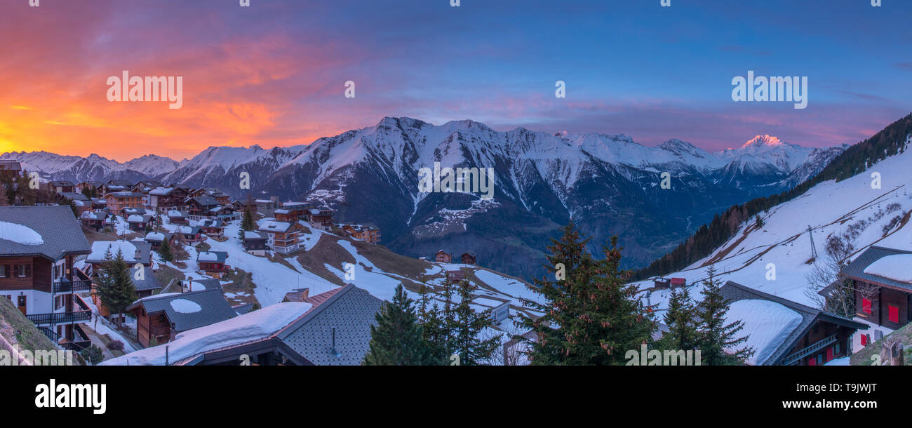 Panoramic view of snowcapped mountain range at sunrise. Swiss Alps at sunrise, mountain town with colorful sky. Stock Photo