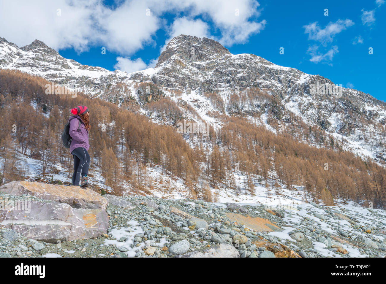 Mountain girl, female hiker with a hat contemplates the snowcapped mountains of Switzerland. Girl hiking in the snow. Stock Photo