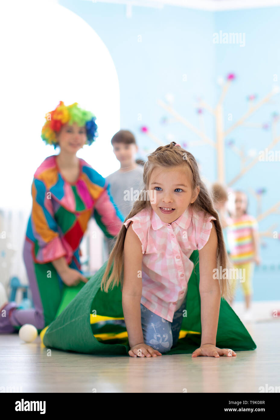 Children kids playing with clown on birthday party in entertainment centre. Little girl climbing through tunnel Stock Photo