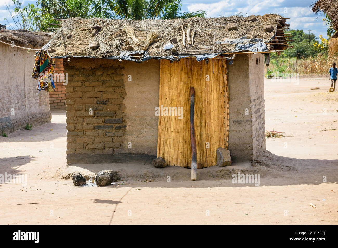 a small mud hut with a grass roof and a door made from a reed mat in a village in Malawi Stock Photo