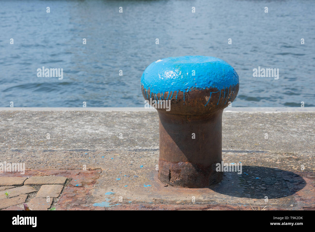 A blue painted bollard on the side of the water Stock Photo