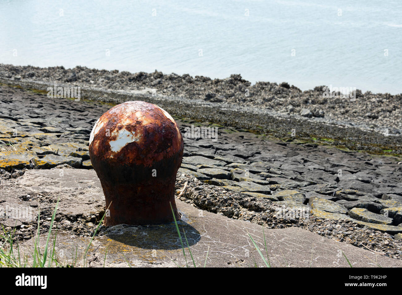 Old rusty bollard with a little white paint and in the background the sea Stock Photo