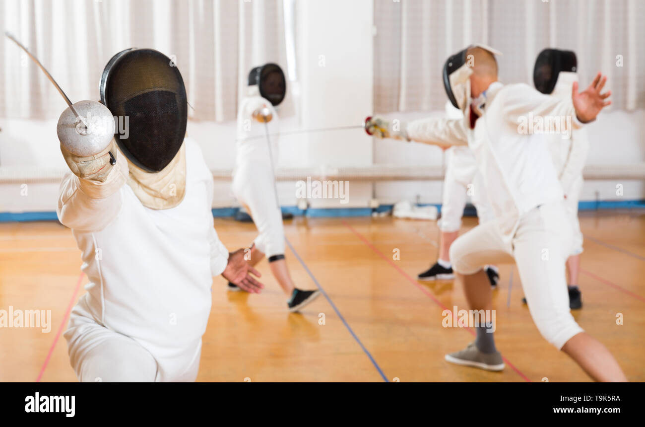 Closeup portrait of positive fencer in mask practicing lunge with foil