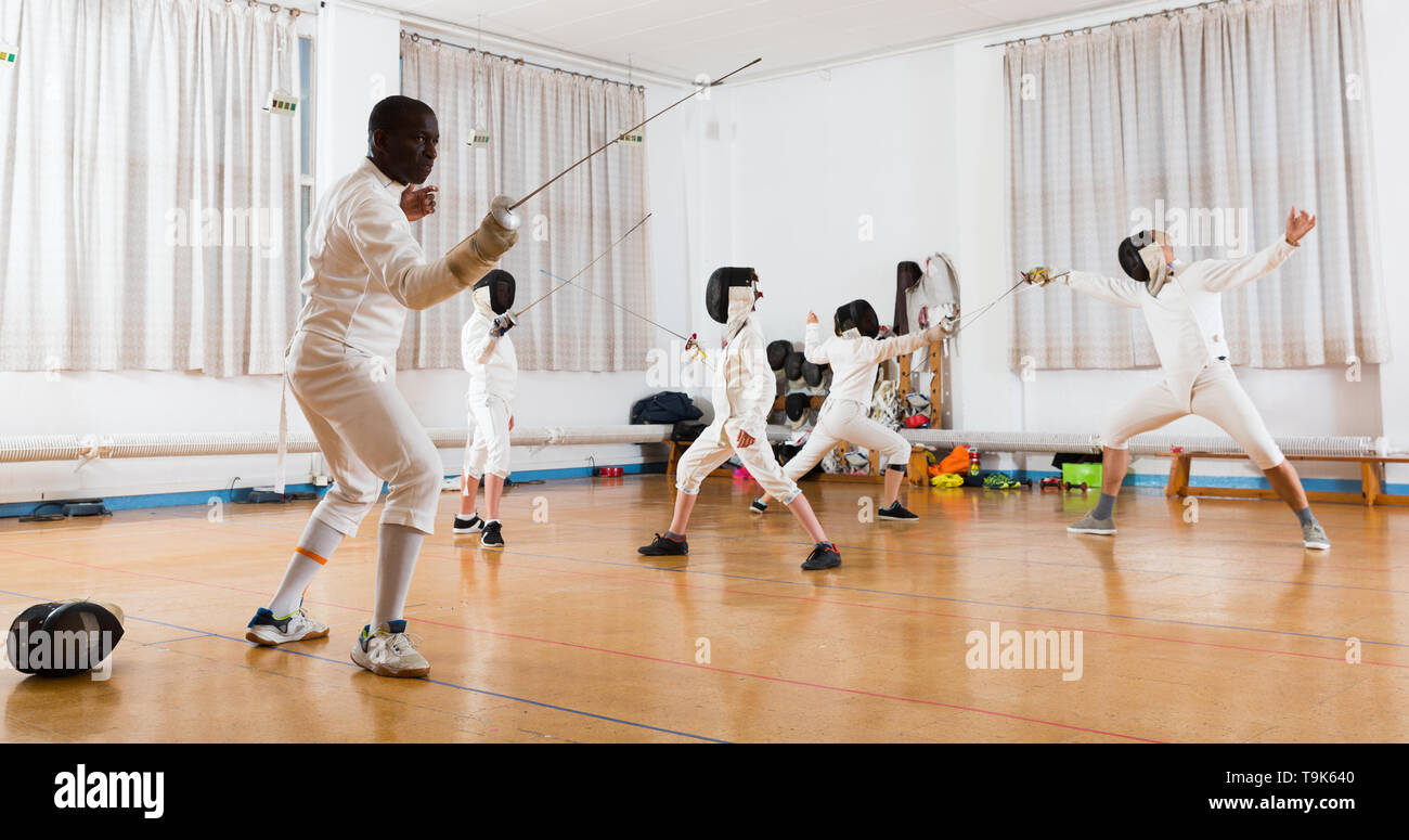 adults and children athletes at fencing workout, training attack movements in duel Stock Photo