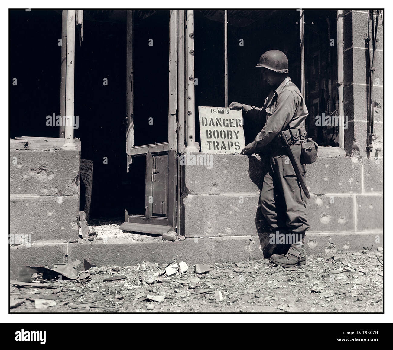 WW2 1940's archive image of American GI soldier placing a 'Booby Traps' warning notice on a French war damaged house Perriers-en-Beauficel Normandy France August 11 1944 American Baker Company Stock Photo
